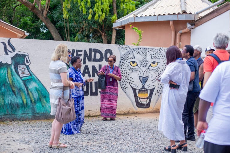 Groupe de voyageurs devant une fresque vodun a la panthere, Ouidah