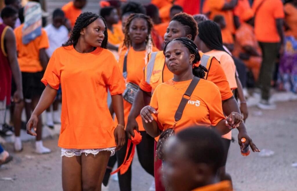 Young women in orange T-shirts walking in a Fetu Afahye procession through the streets of Cape Coast, Ghana