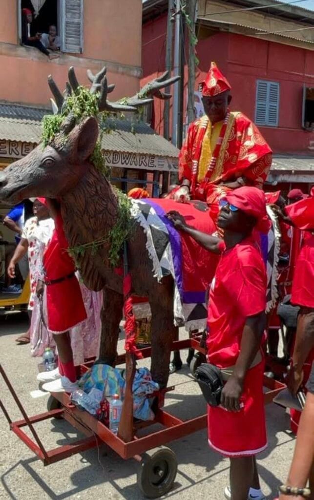 A wheeled float carrying a sculpted deer, a dignitary in red robes and cap seated on it, during Fetu Afahye in Cape Coast
