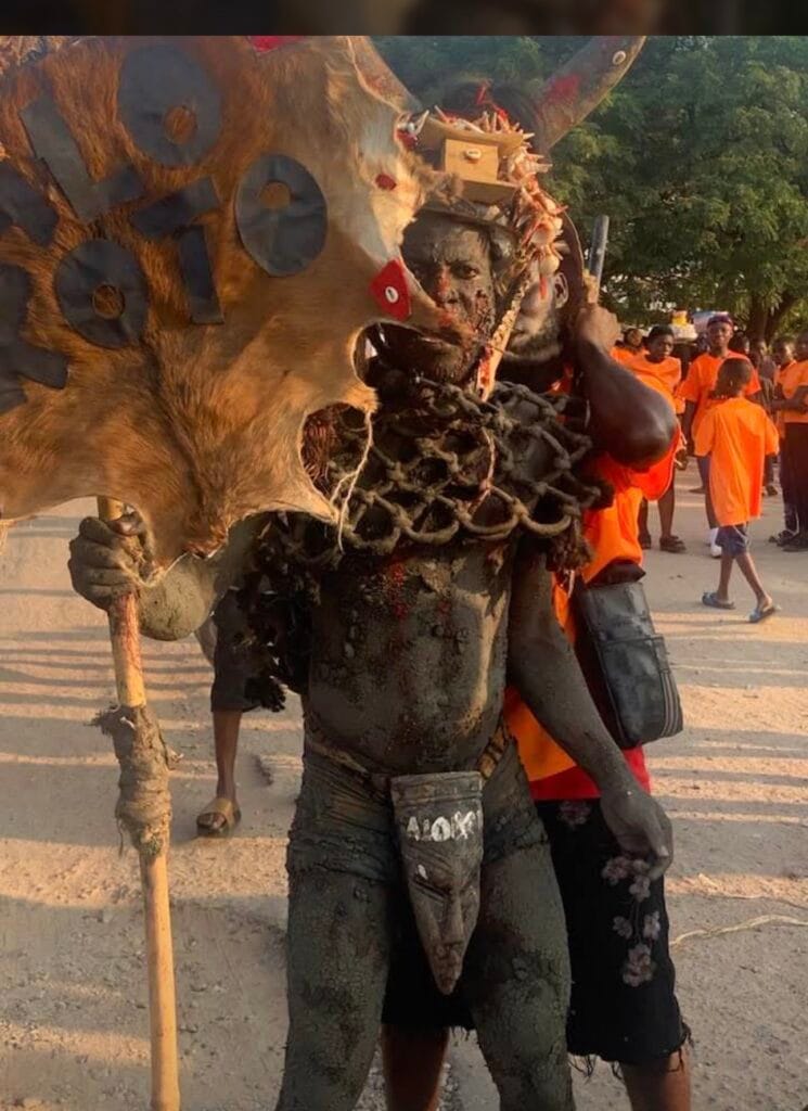 Masked figure in blackened body paint carrying an animal hide and shield during Fetu Afahye, Cape Coast